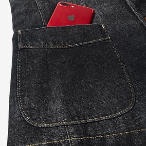 Gros plan sur la poche poitrine d'une veste en jean noire avec coutures dorées