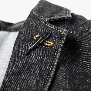 Détail macro d'une broche plume noir mat épinglée sur le revers d'une veste en jean