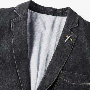 Détail d'un blazer en jean noir délavé avec coutures jaunes et broche en forme de plume fine
