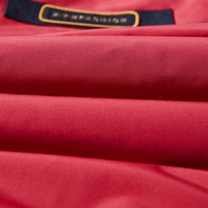 Dettaglio macro del tessuto rosso per giacca imbottita con nastro nero ricamato X-Y-NFASHION