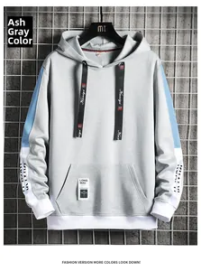 Détail d'un sweat gris avec manches bleues, poche kangourou et cordon sur fond industriel