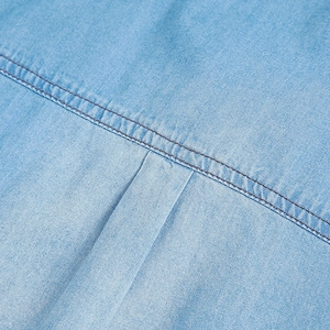 Detailed macro view of light blue denim shirt showing dual stitching and pleated fabric texture