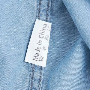 Close-up of light blue denim shirt fabric with a clear wash label and white stitching