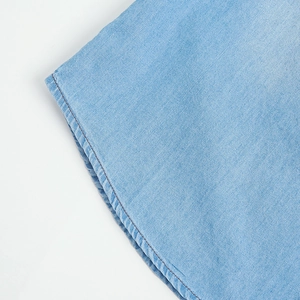 Detail of light blue denim shirt showing a curved hem and clean stitching lines