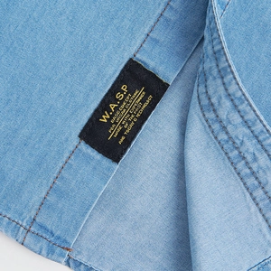 Detailed macro view of denim shirt stitching with woven brand label on light blue cotton fabric