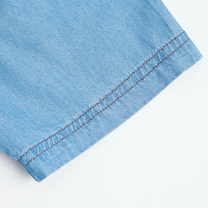Detail of light blue denim shirt showing dual brown stitching and breathable cotton fabric