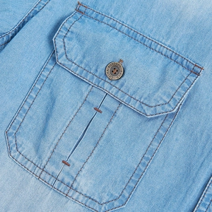 Detailed close-up of light blue denim shirt pocket with vintage metal button and orange stitching