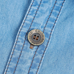 Detailed macro view of vintage metal button and contrast stitching on blue denim shirt
