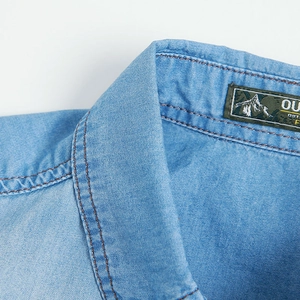 Close-up of light blue cotton denim shirt collar with brown stitching and outdoor label
