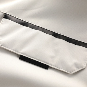 Detail der beigen Kapuzenjackentasche mit schwarzem Kontraststreifen und kleinem Webeetikett