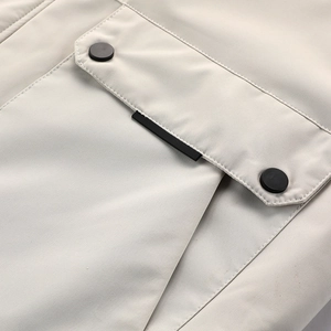 Detailansicht einer beige Kapuzenjacke mit Klappentaschen und schwarzen Metalldruckknöpfen