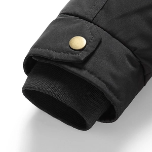 Dettaglio del polsino antivento di un parka nero da uomo con bottone a pressione in metallo dorato