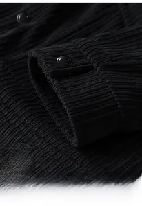 Detail of black corduroy jacket sleeve featuring metallic snap button and textured fabric