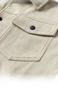 Macro detail of beige corduroy jacket showing breast pocket with black button and soft texture