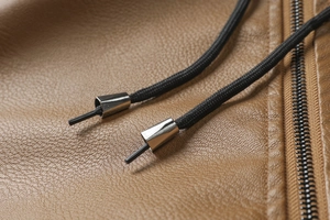 Detail of brown faux leather jacket featuring black zipper and drawstring with metal tips