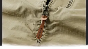 Detail of khaki outdoor jacket featuring metal zipper and leather tab with outdoor lettering