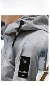 Detailed view of grey hooded jacket featuring drawstring and sleeve patch with typography