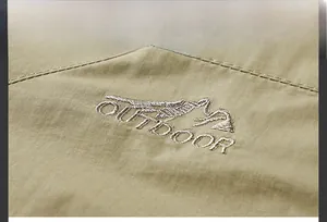 Macro view of khaki outdoor jacket featuring detailed mountain embroidery on fabric