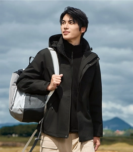 Detail of men's black 3-in-1 outdoor jacket with windproof hood and gray hiking backpack