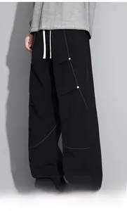 Détail du pantalon cargo noir avec coutures orange, rivets et cordon de serrage blanc