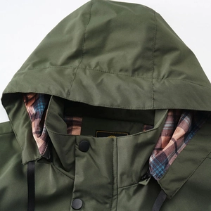 Detail of dark green outdoor jacket featuring windproof fabric and blue-brown tartan lining