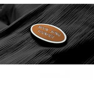 Detail of black pleated corduroy fabric with a brown Moon Song Founder branded patch