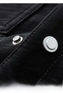 Macro detail of silver 3D metal press studs on a black textured knit fabric jacket