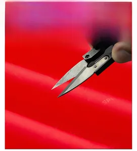 Detail showing the scratch-resistant red fabric of an outdoor jacket tested with metal scissors
