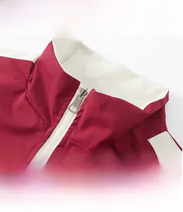 Gros plan du col montant et du zip métallique sur la veste de sport rouge avec bordure blanche