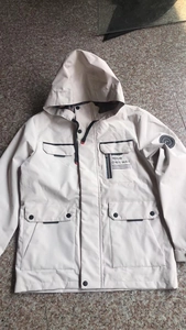 Detail of beige hooded parka featuring large flap pockets and mountain badge on sleeve