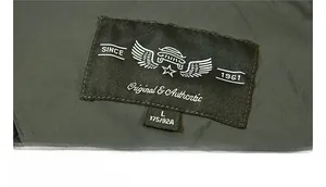Detailed view of the olive green windbreaker collar label with vintage embroidered logo