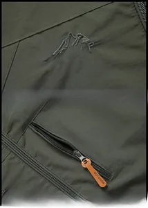 Detail of army green outdoor jacket featuring mountain embroidery and leather zipper pulls