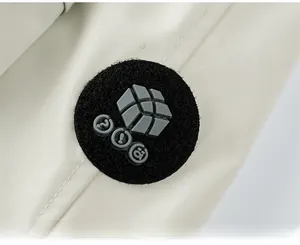 Dettaglio ravvicinato della toppa logo in silicone nero su tessuto giacca bianco