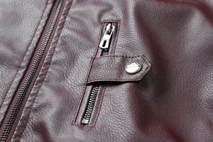 Détail de la texture cuir synthétique bordeaux avec fermeture éclair et bouton pression