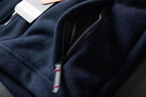 Detailed close-up of dark blue fleece jacket showing zipper pocket with decorative cord