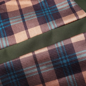 Macro detail of men's jacket featuring plaid fabric texture and durable green strap