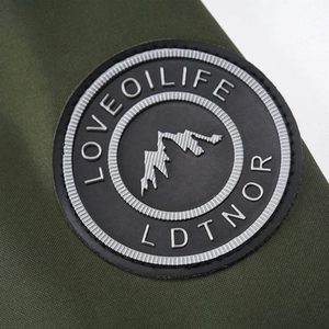 Detail of mountain logo patch on dark green outdoor jacket with embossed textured fabric