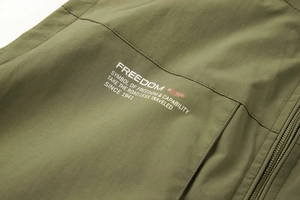 Close-up of olive green fishing vest fabric with white text and logo prints