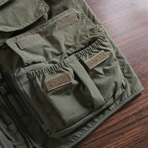 Detail view of army green tactical vest featuring a large cargo pocket with velcro closure