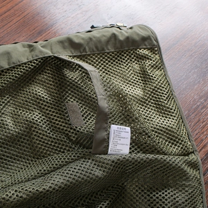 Detail of army green mesh pocket with velcro closure and white washing instruction label
