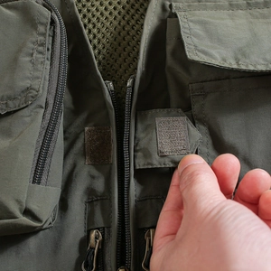 Detail of military green tactical vest showing zipper, velcro pockets and mesh lining