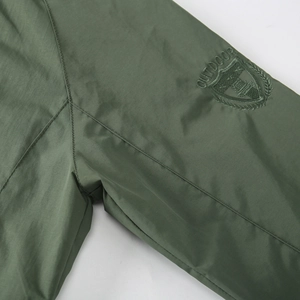 Detailed close-up of embroidered outdoor badge on dark green hooded windbreaker jacket