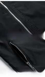 Detail einer Herrenjacke mit gesticktem Slogan und metallischer Reißverschlusstasche