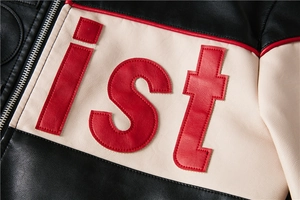 Detailed close-up of beige faux leather jacket featuring red ist letter embroidery and metal zipper