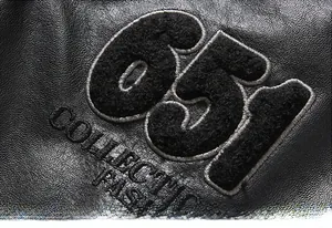 Detailaufnahme der Lederjacke mit schwarzer Handtuch-Stickerei 651 und dem Markenlogo
