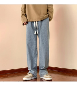 Detail of light blue washed denim jeans featuring a white drawstring waist and relaxed fit