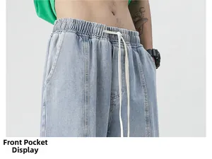 Detail of elastic drawstring waistband and front pocket on light blue denim jeans