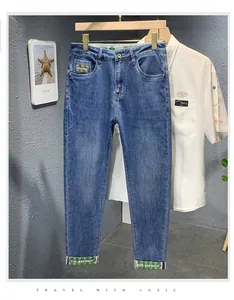 Détail du jean bleu coupe droite avec ruban rayé vert et broderie de lettres décorative