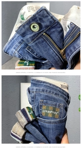Détail d'un jean denim bleu foncé avec bouton en métal, zip et poche à broderie damier