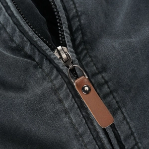 Detail view of silver metal zipper with vintage brown leather pull on a gray cotton jacket